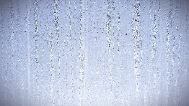 Raindrops trickling down glass in window