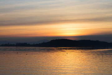 Obraz premium A shoot of a sunset over a lake, with many striped, diagonals clouds