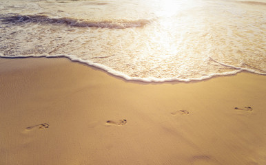 Beach, wave and footprints at sunset time