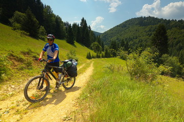 Obraz premium A tourist with a bicycle on a way with mountain meadows