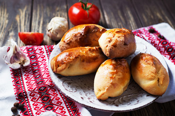 Hearty and tasty food, national Ukrainian cuisine, pies from yeast dough with cabbage, tomatoes and spices on rushnyke on a dark wooden background