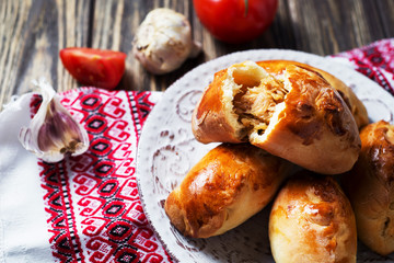 Hearty and tasty food, national Ukrainian cuisine, pies from yeast dough with cabbage, tomatoes and spices on rushnyke on a dark wooden background