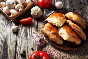 Hearty and tasty food, national Ukrainian cuisine, pies made of yeast dough with mushrooms, tomatoes and spices on rushnyk on a dark rustic wooden background  