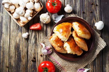 Hearty and tasty food, national Ukrainian cuisine, pies made of yeast dough with mushrooms, tomatoes and spices on rushnyk on a dark rustic wooden background  