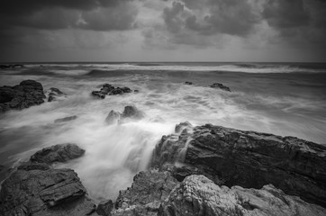 Black and white image, beautiful nature wave hitting the rock over dramatic cloudy sky