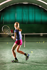 Young girl plays tennis at indoor court