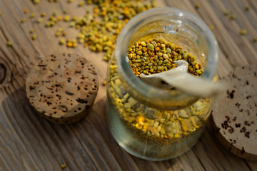 Grains of bee pollen in jar and wooden spoon on wooden table . Apitherapy. Bee products.