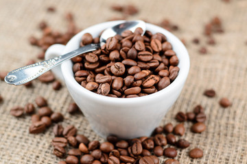 Cup full of coffee beans on the cloth sack background