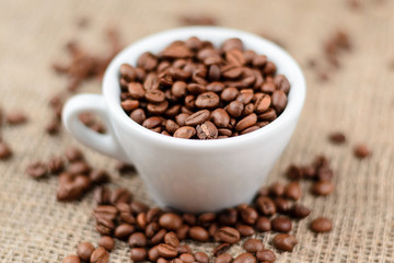 Cup full of coffee beans on the cloth sack background