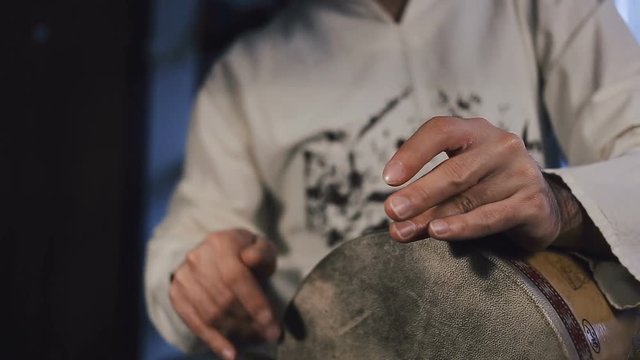 close up shot of man drumming out a beat on an arabic percussion drum named Tombak at home. Shot with other percussian drums on background.