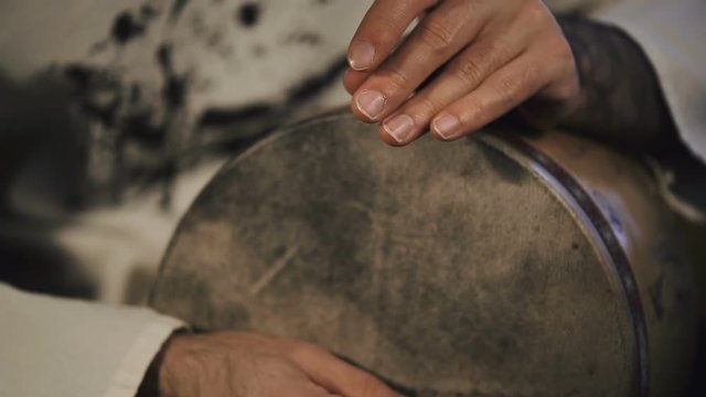 close up shot of man's hands drumming out a beat on an arabic percussion drum named Tombak at home.