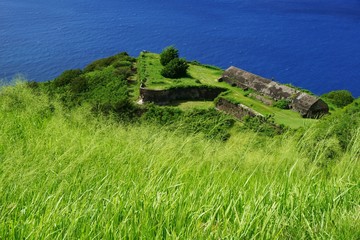 Fototapeta na wymiar Brimstone Hill Fortress fortifications and buildings with green grass and bright blue sea