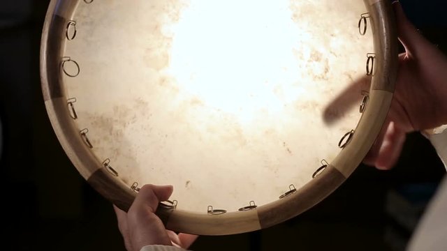 close up shot of man drumming out a beat on an arabic percussion drum named Dayereh at home. Shot at counterlight.