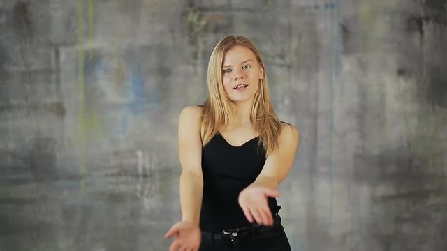 Beautiful blond hair teen girl dancing hiphop on the gray wall. Actively works with hands.