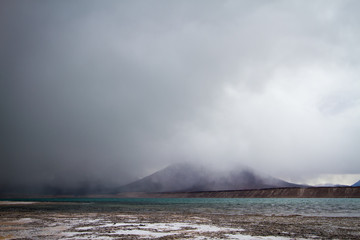 Green lagoon with low clouds next to a volcano, on the border between Chile and Argentina