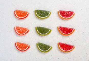 Fruit jelly in the form of citrus fruits are divided by color into three rows and three bars on a gray table top
