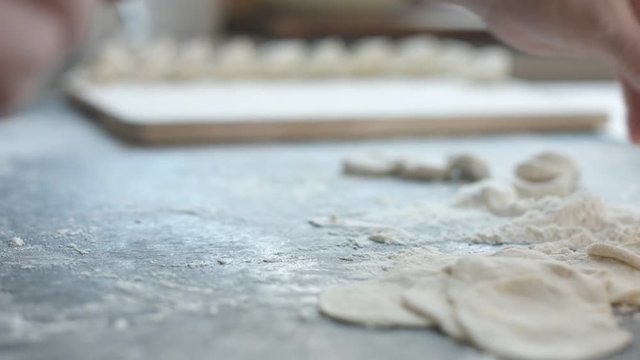 Side view of two woman's hands making meat dumpling with wooden rolling pin.