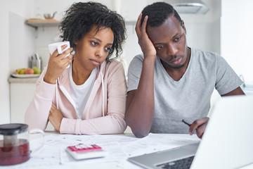 Young african american family, sitting at kitchen table. feeling unhappy because financial problem and economic crisis, trying to solve troubles, reviewing their finances using online bank application