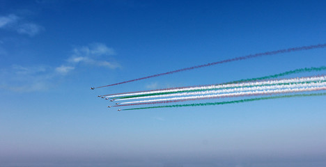 Group of airplanes with colored track red, white, green clouds on blue sky background, horizontal view. Colors of italian flag.