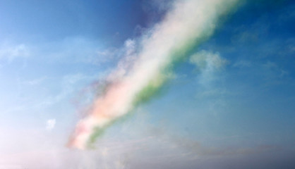 Colored red, white and green clouds, track of airplane on blue sky background, horizontal view. Colors of italian flag.