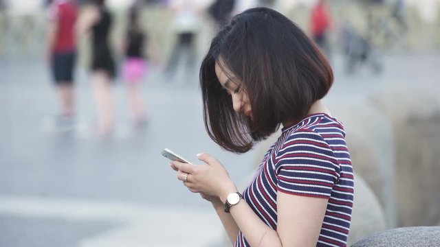 Profile of young Chinese woman while using her smartphone