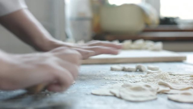 Side view of two woman's hands making meat dumpling with wooden rolling pin.