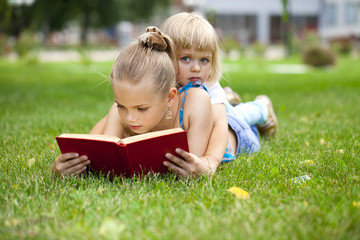 Adorable cute little girl reading book outside on grass