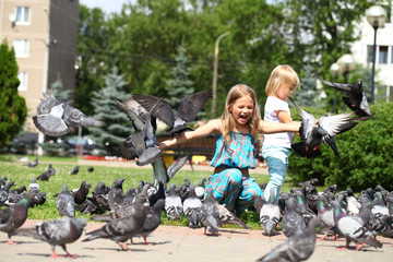 Happy little girl feeding doves in the city street