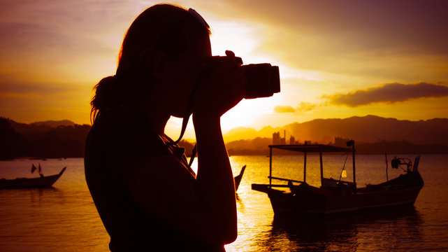 Girl taking a photo with a DSLR digital camera of the beach during sunset in tropical Langkawi island, Malaysia