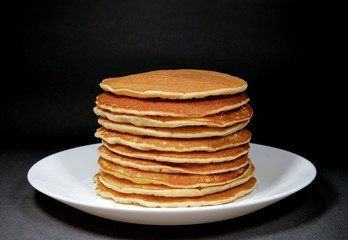 Piled up homemade plain pancakes served on white plate, isolated on black background 