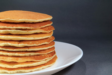 Stack of fresh homemade plain pancakes served on white plate, isolated on black background 