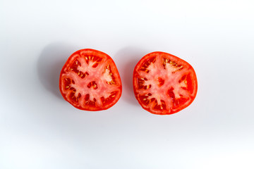 Tomatoes cut In halves on white table with natural shadows.