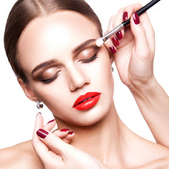 Professional makeup artist applies makeup for beautiful young woman with blue eyes and light brown hair style and perfect skin. studio shot, isolated on white background.