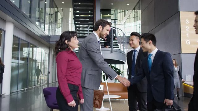  2 Business groups meet & shake hands in large modern office building