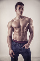 Fototapeta premium Handsome young muscular man shirtless wearing jeans, on dark background in studio shot