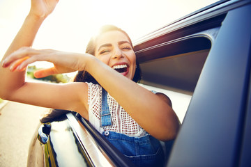 Woman seated in car waves her arms and laughs