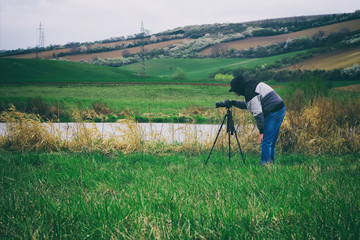 Photographer with a tripod photographing landscapes. Man takes picture near to a small lake in the countryside.