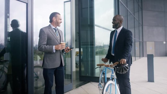  Businessman with bicycle leaving office building & talking to coworker