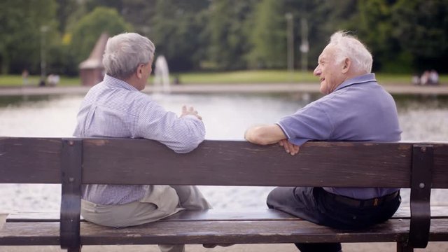  Happy senior male friends chatting in the park & looking out at view of lake