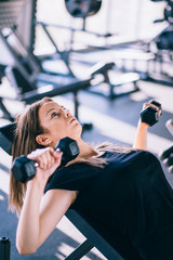 Young beautiful woman doing exercises with dumbbell in gym.