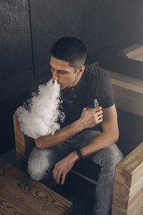 Vaping man holding a mod. A cloud of vapor. Black background. Smoking electronic cigarette Vape advertisement concept