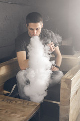 Vaping man holding a mod. A cloud of vapor. Black background. Smoking electronic cigarette Vape advertisement concept