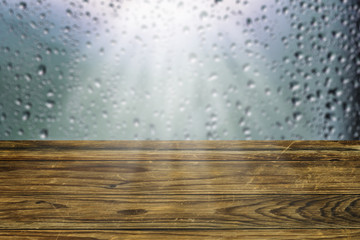 Empty rustic wooden board or old weathered garden table top blurred window with raindrops.