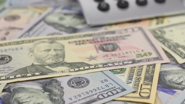 Dolly shot, focus on dollars, calculator lying on the table.