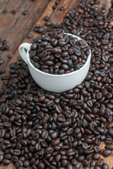 Close up shot of dark roasted coffee bean in white ceramic cup on wooden floor with copy space