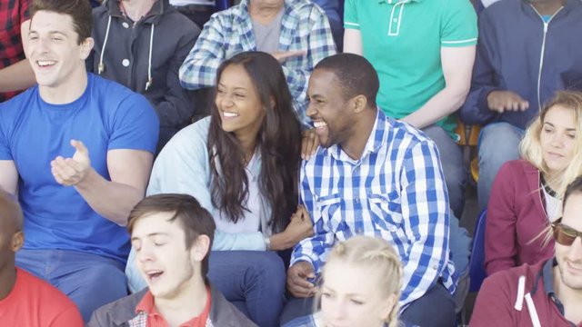  Crowd cheering on their team at sports event, focus on young couple