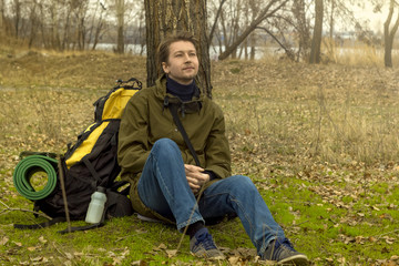 Naklejka na ściany i meble Active people. Outdoors. Traveler. Tourist. Sitting guy. A man with a backpack. Near a tree.