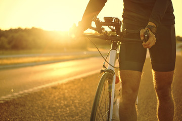 Naklejka na ściany i meble Man holding bicycle on empty sunset road