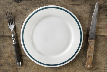 Small, empty plate, fork and knife on old wooden chopping board