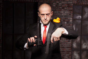 Angry contract murderer aims a pistol on toy duck